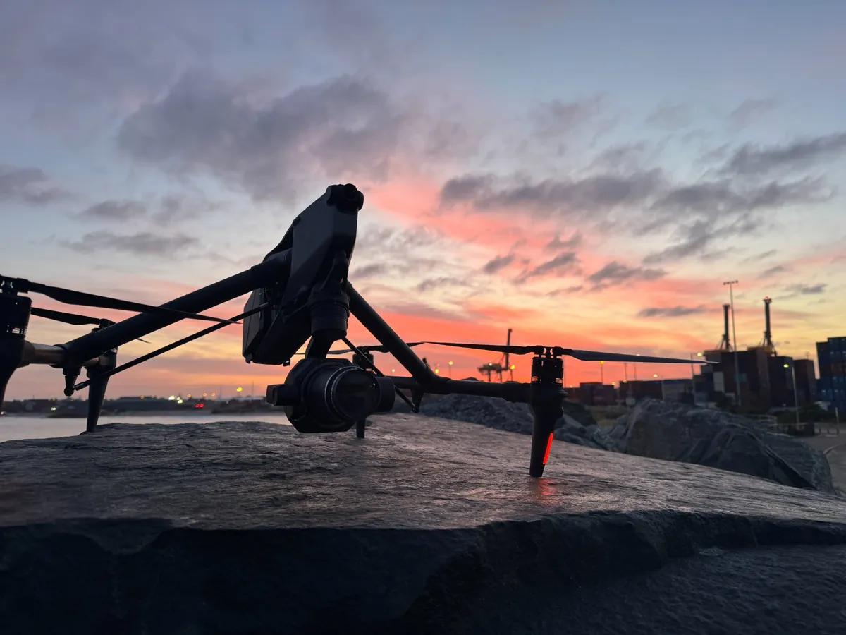 DJI Inspire 3 cinema drone silhouetted on a Fremantle breakwater against a pink sunrise, with the port cranes on the horizon